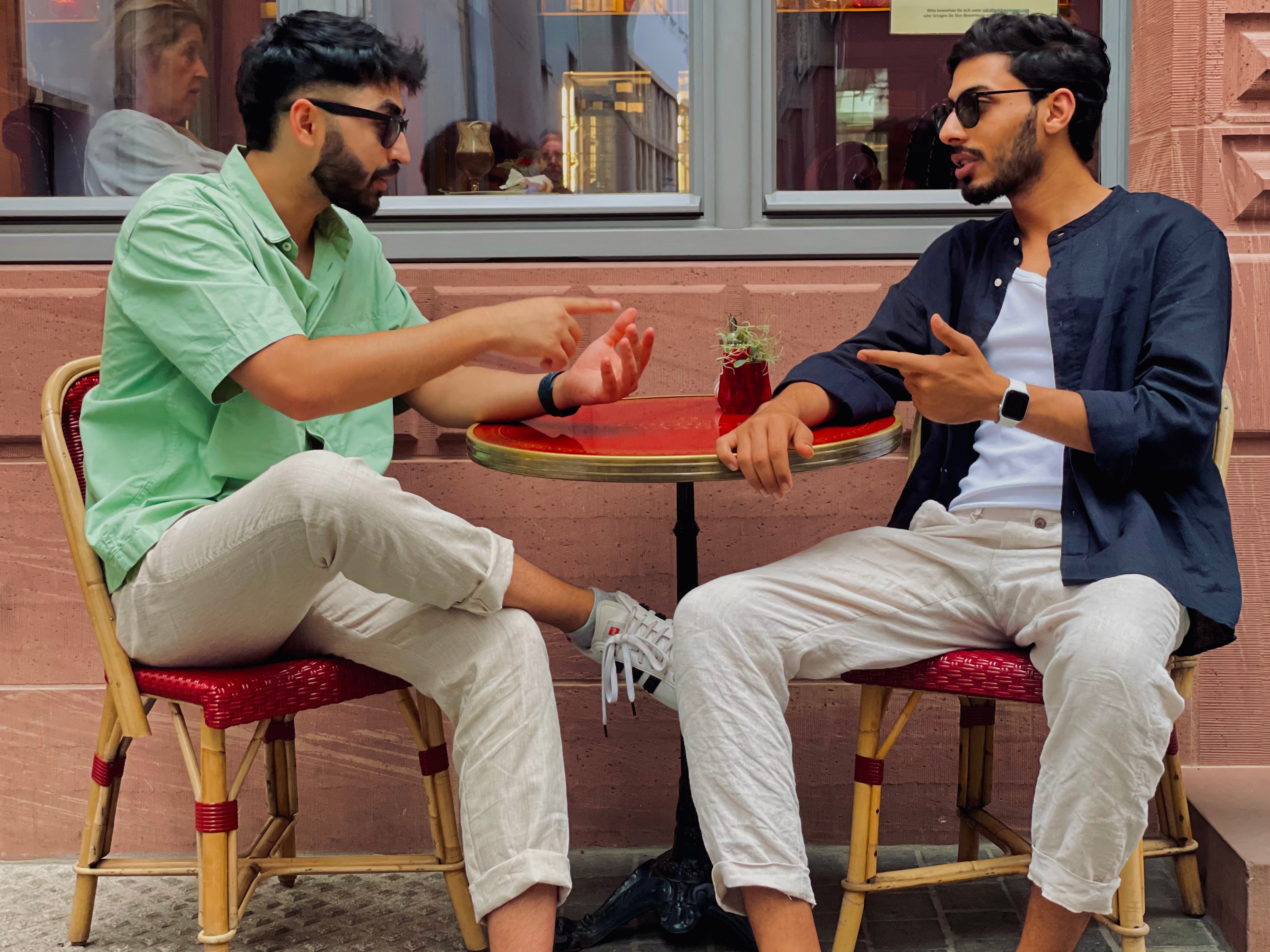 Two men sitting at a small table in an outdoor cafe setting.